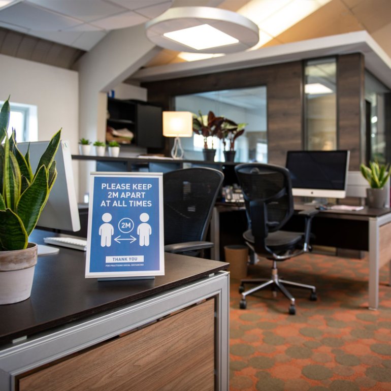 Desk in an office environment with an Absolute Freestanding Label Holder to display social distancing rules.  Desk in an office environment with an Absolute Freestanding Label Holder to display social distancing rules.